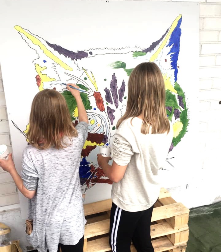 Kaksi lasta maalaa suurta Leo-kissan kasvokuvaa seinätaululle.